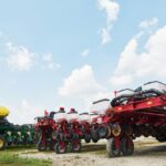 Un agriculteur moderne gérant ses opérations via un smartphone, avec un tracteur et des balles de foin en arrière-plan, symbolisant la digitalisation de l'agriculture et l'utilisation des "machines agricoles"