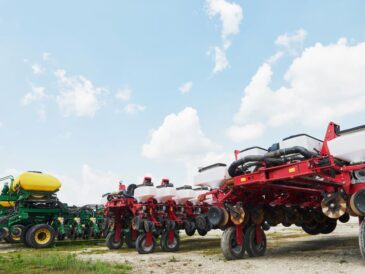 Un agriculteur moderne gérant ses opérations via un smartphone, avec un tracteur et des balles de foin en arrière-plan, symbolisant la digitalisation de l'agriculture et l'utilisation des "machines agricoles"