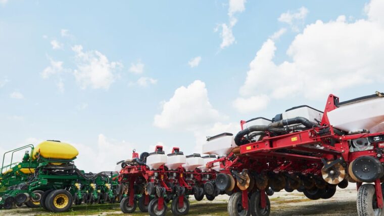 Un agriculteur moderne gérant ses opérations via un smartphone, avec un tracteur et des balles de foin en arrière-plan, symbolisant la digitalisation de l'agriculture et l'utilisation des "machines agricoles"