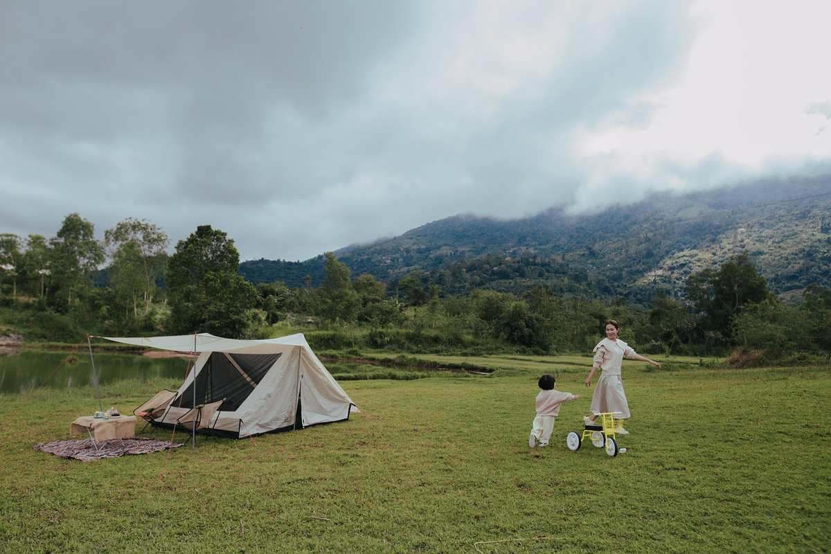 Une tente dressée dans un pré avec deux enfants jouant près d'une rivière et montagnes en arrière-plan Une tente dressée dans un pré avec deux enfants jouant près d'une rivière et montagnes en arrière-plan
