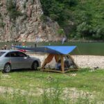 Camping aménagé au bord d'une rivière avec voiture et tente bleue