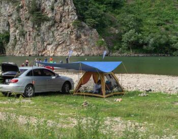 Camping aménagé au bord d'une rivière avec voiture et tente bleue