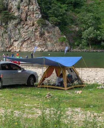 Camping aménagé au bord d'une rivière avec voiture et tente bleue