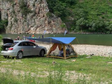 Camping aménagé au bord d'une rivière avec voiture et tente bleue