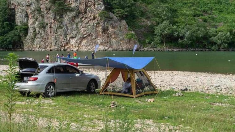 Camping aménagé au bord d'une rivière avec voiture et tente bleue