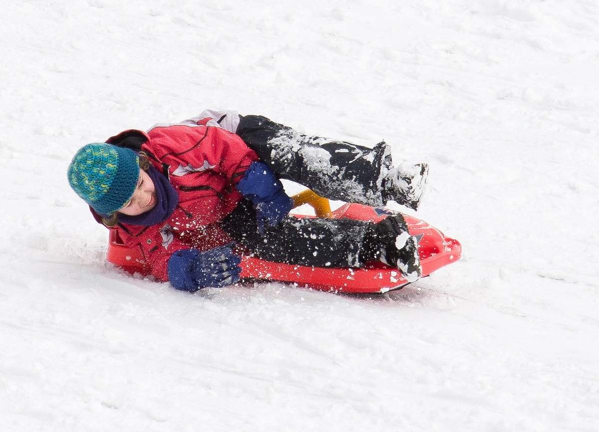 Un enfant en manteau rouge glisse sur un traîneau rouge dans la neige Un enfant en manteau rouge glisse sur un traîneau rouge dans la neige