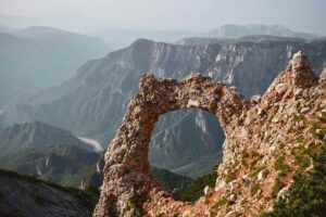 Un arc naturel de pierre se détache sur un décor montagneux