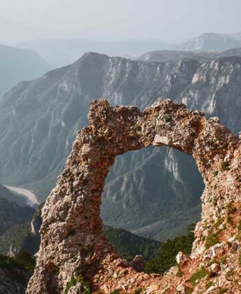 Un arc naturel de pierre se détache sur un décor montagneux