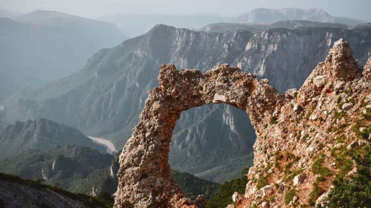 Un arc naturel de pierre se détache sur un décor montagneux