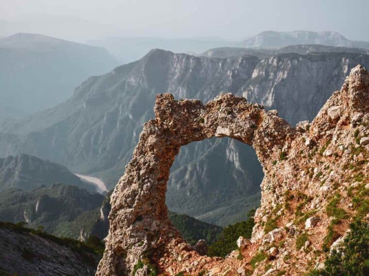Un arc naturel de pierre se détache sur un décor montagneux