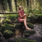 woman in purple and black floral dress sitting on rock in river