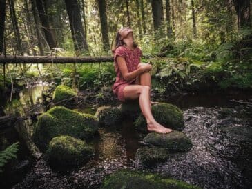 woman in purple and black floral dress sitting on rock in river