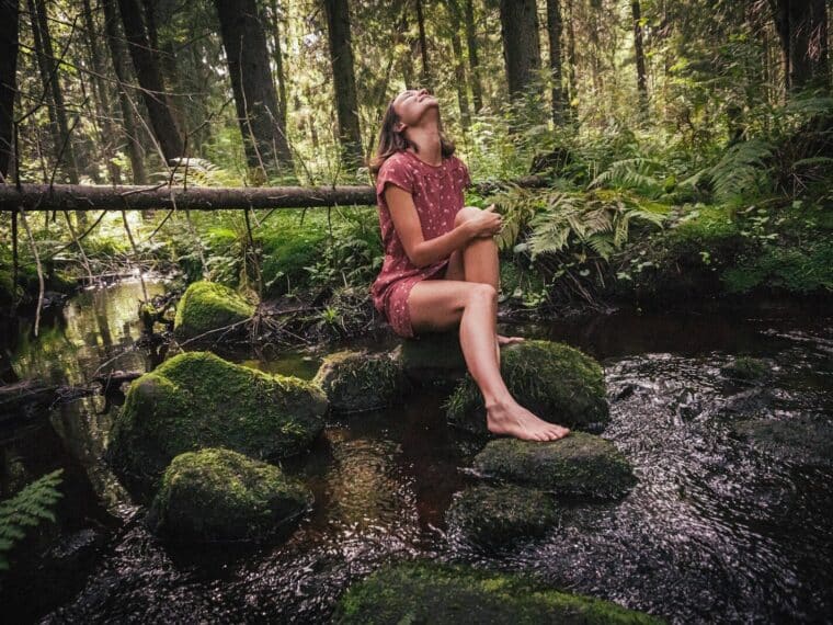 woman in purple and black floral dress sitting on rock in river